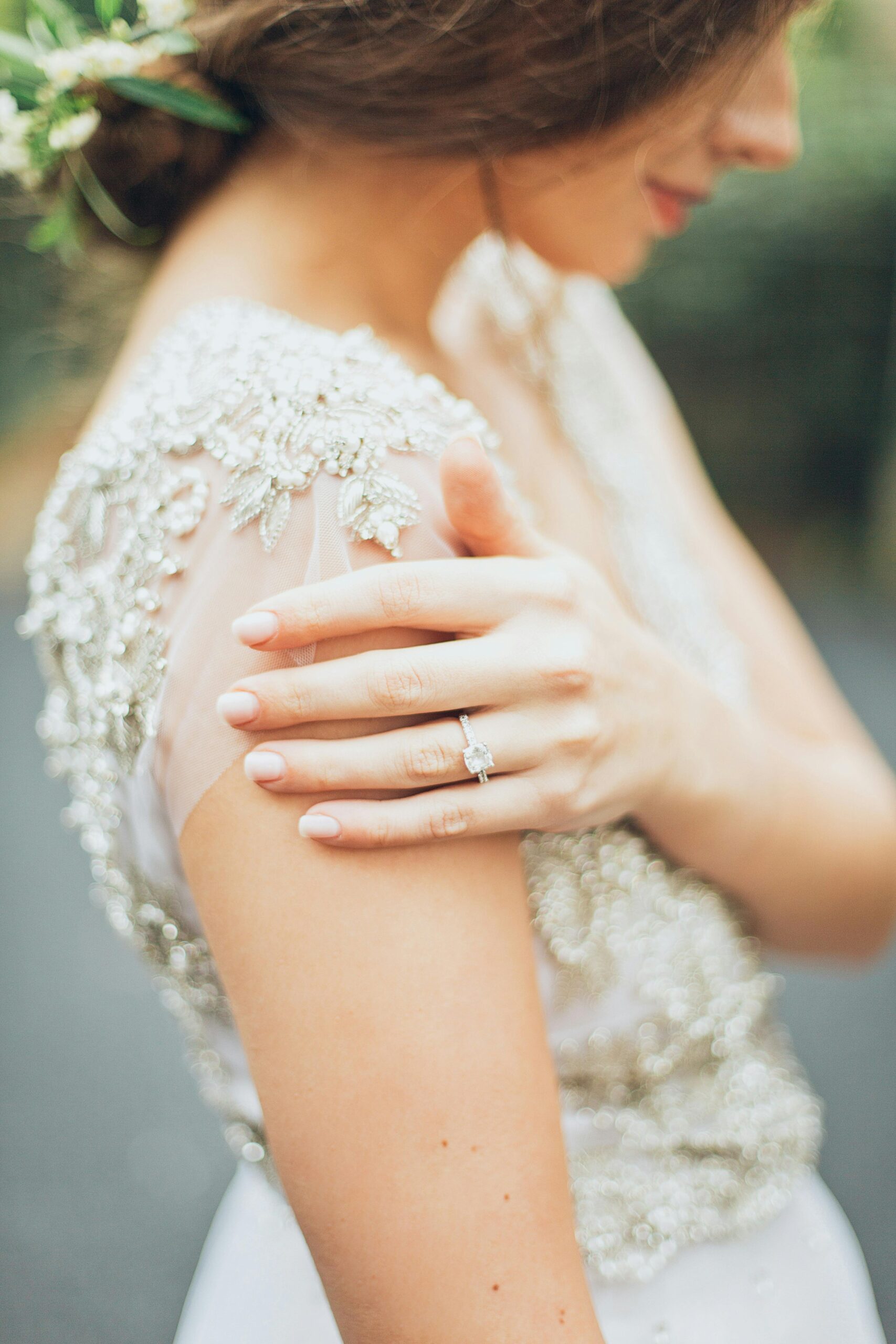 Home Close-up of a bride showcasing a wedding ring and intricate gown details outdoors.